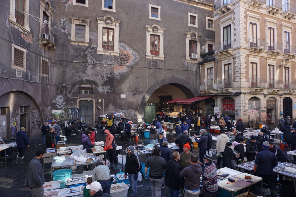 Catani'a fish market, showing white tables full of fish and crowds of people standing around in a town square.