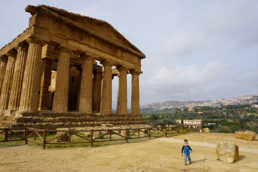 young boy running in front of remains of a greek temple in agrigento, sicily.