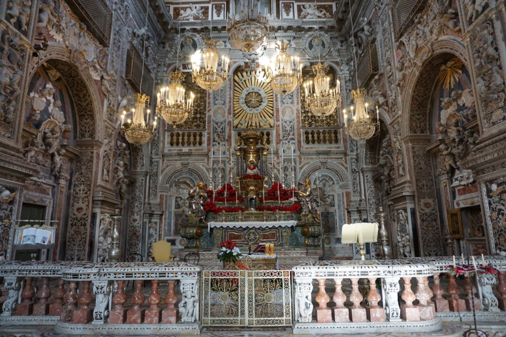 Ornate church altar with pink marble columns and gold inlay and chandeliers.