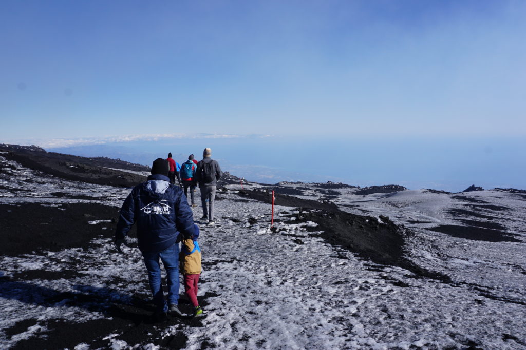 man and child walking along snow covered top of mount etna volcano.