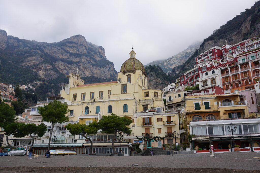 Photo of the city of Positano on the Amalfi Coast in Italy. The mosaic-domed cathedral stands before fog-covered mountains.