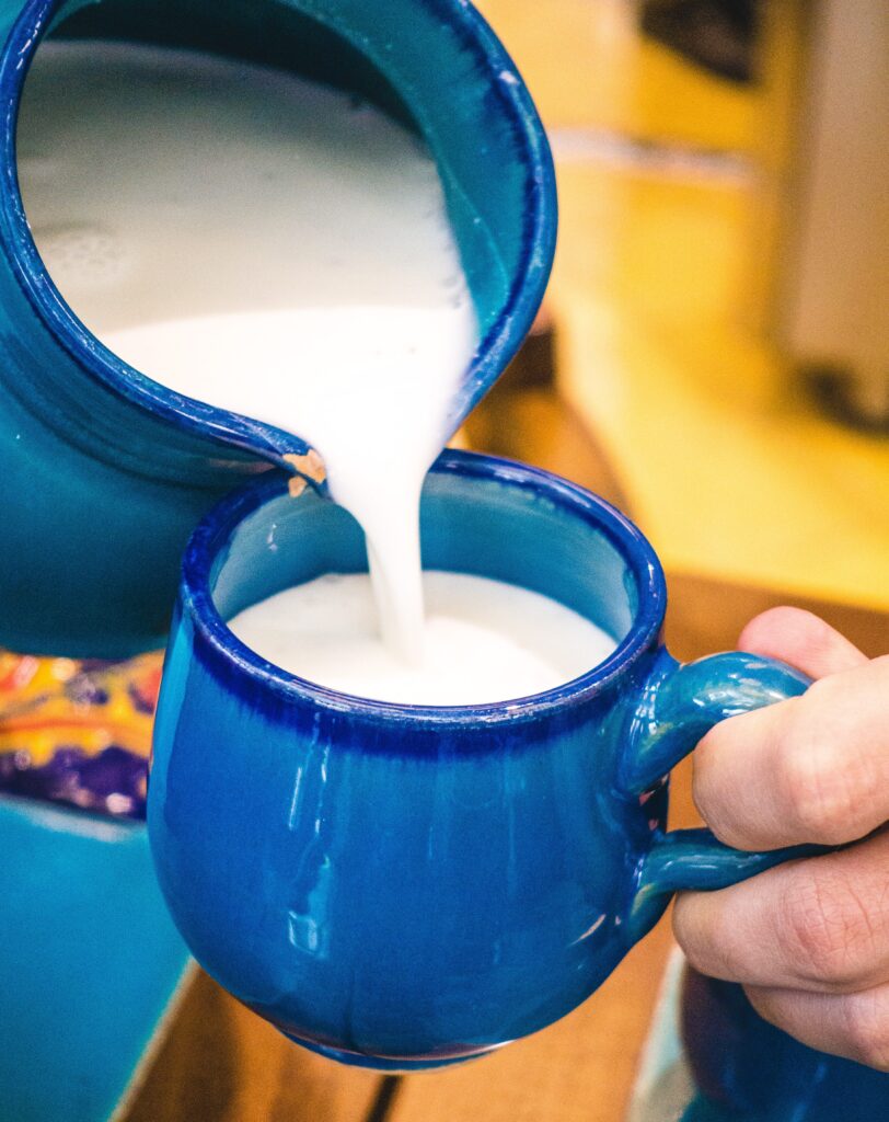 White Turkish yogurt drink ayran being poured from a blue ceramic pitcher into a blue ceramic mug.