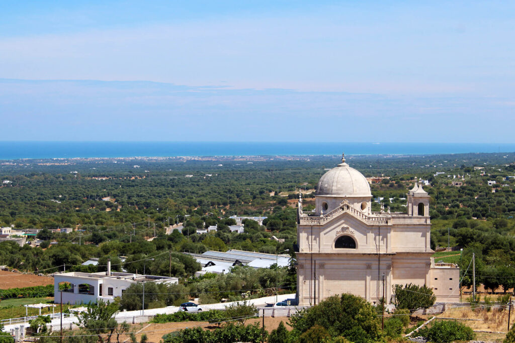 white stone church in front of a flat forested landscape.