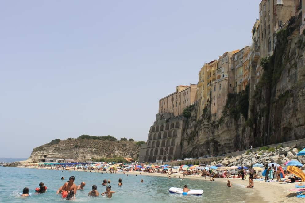 people swimming in the ocean and sunning themselves on the beach.