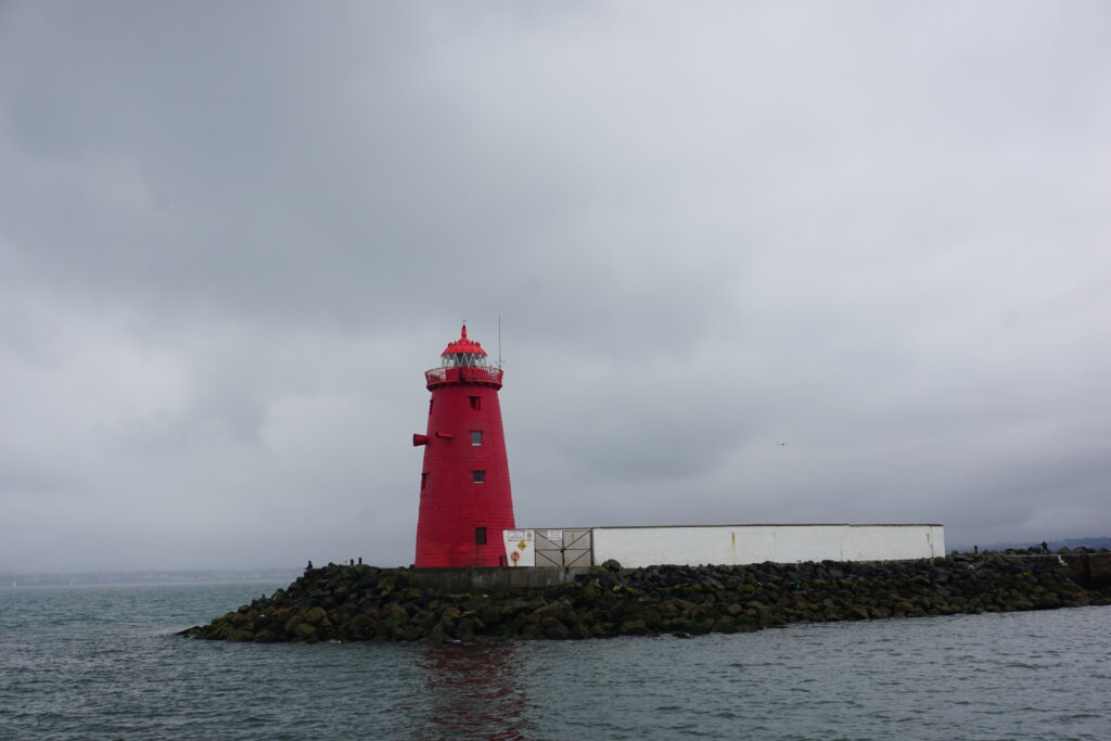 Poolbeg Lighthouse, a small red lighthouse at the end of a stone breakwater in Dublin harbour.