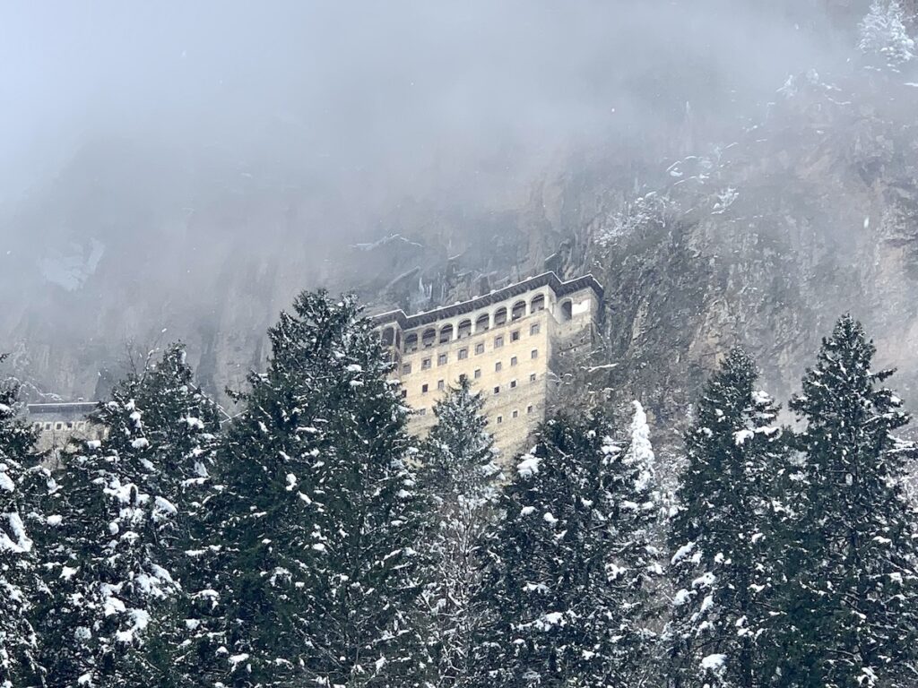 monastery building built into the hillside surrounded by mist and snow capped trees.