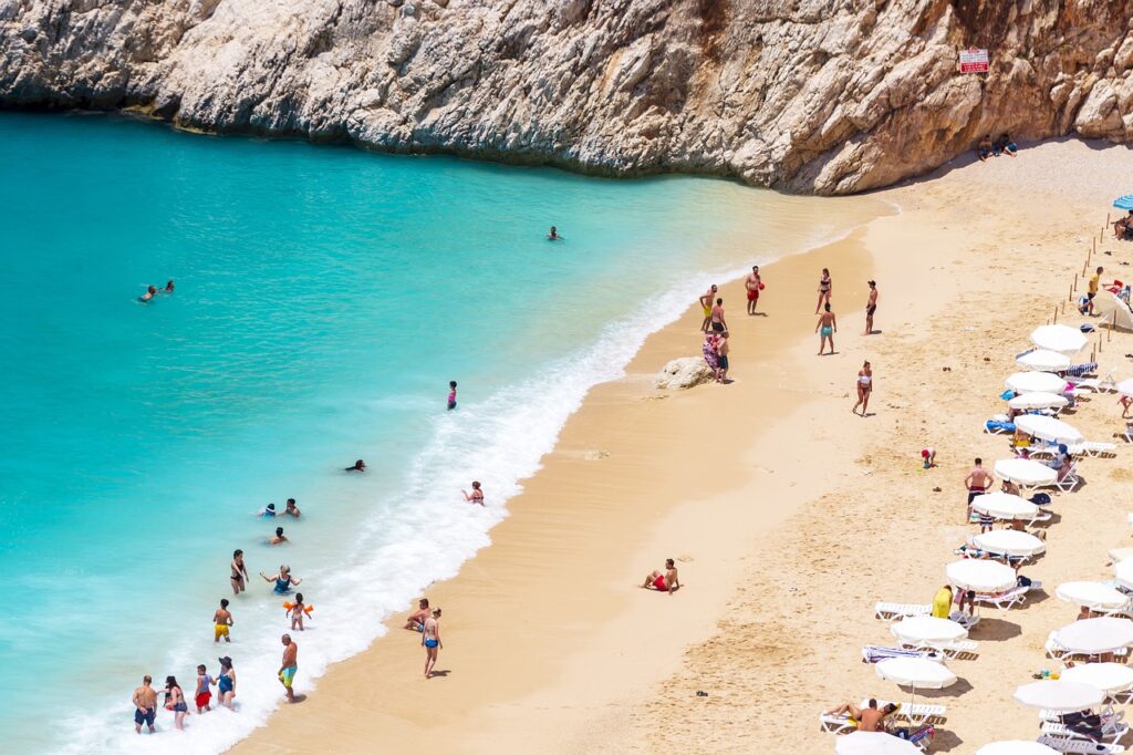 beach with turquoise water and golden sand with people swimming and sunbathing under white umbrellas.