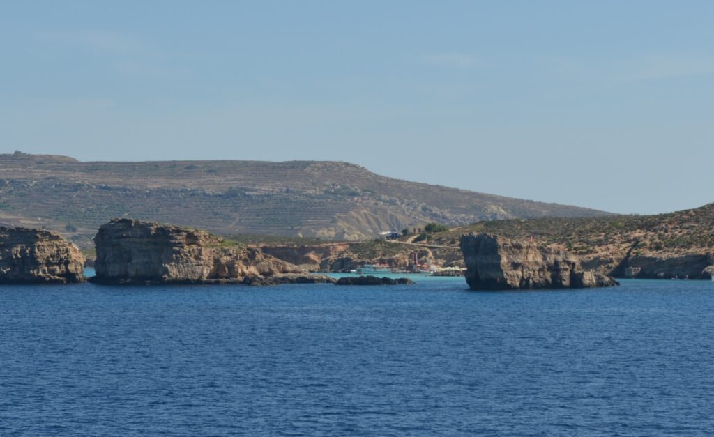 sea water with rocks and boats in the background, hiding the entrance to the blue lagoon in malta