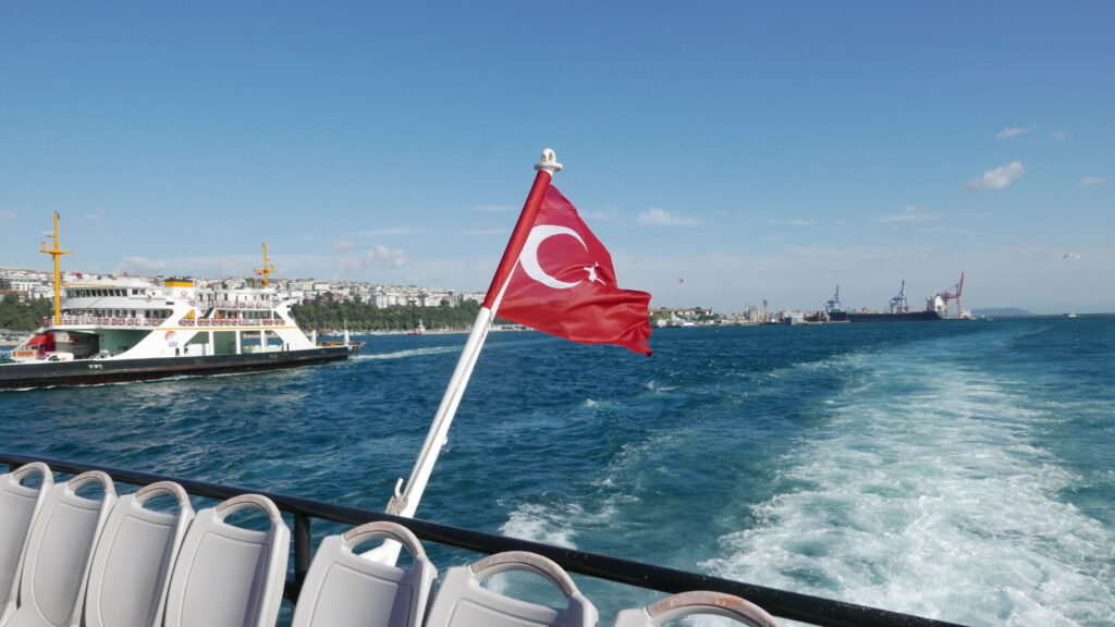 Turkish flag waving on the back of a boat sailing through the water.