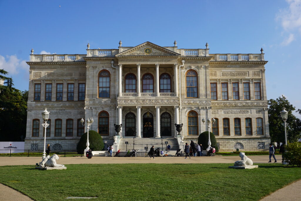 regal dolmabahce palace with white marble entrance and green lawn in front.