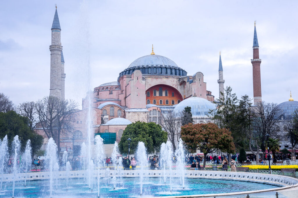 pink colored hagia sophia mosque, one of the most famous landmarks in turkey, with blue dome, four minarets, and fountain in front.