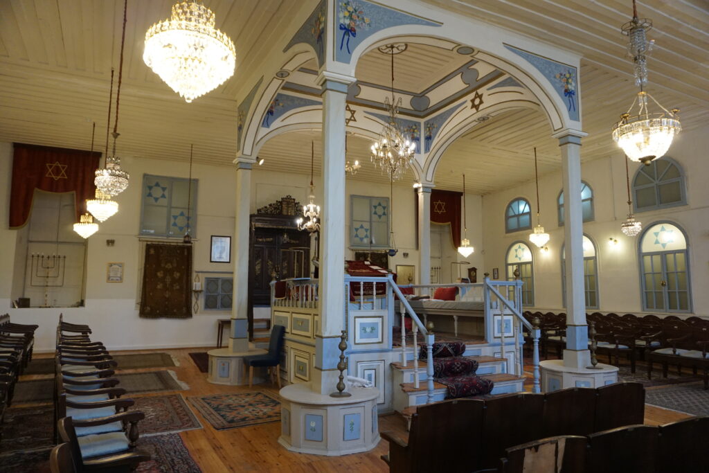 sephardic synagogue in izmir with four white columns central to the room and chairs placed in around it.