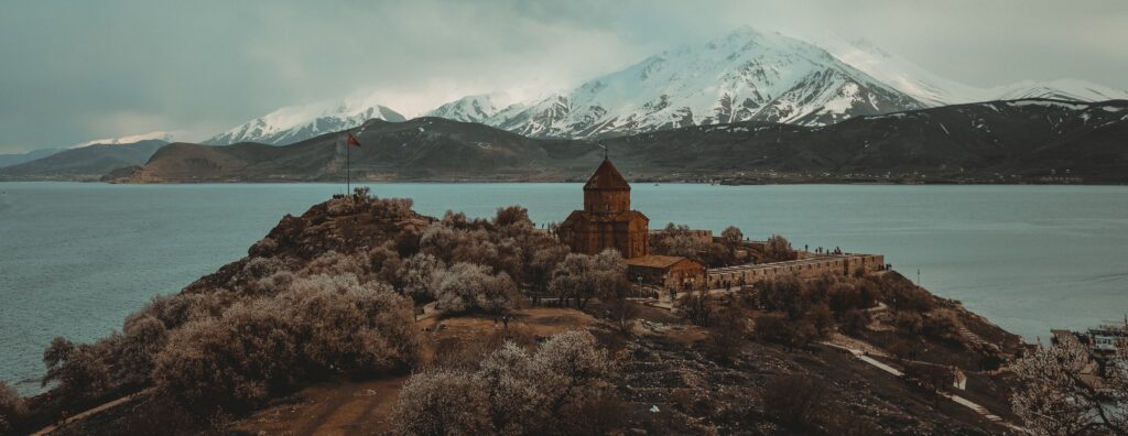 Old Armenian church on a hill in front of a lake with snow-topped mountains in the background.