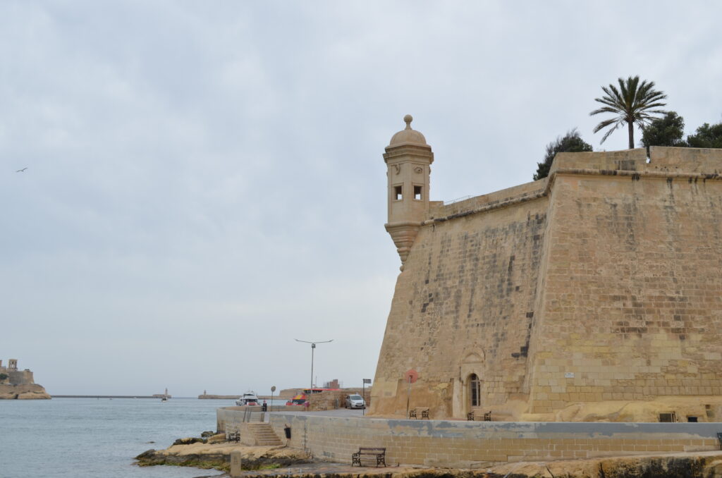 stone defensive wall with a tower sticking out over the water in the Valletta harbor.