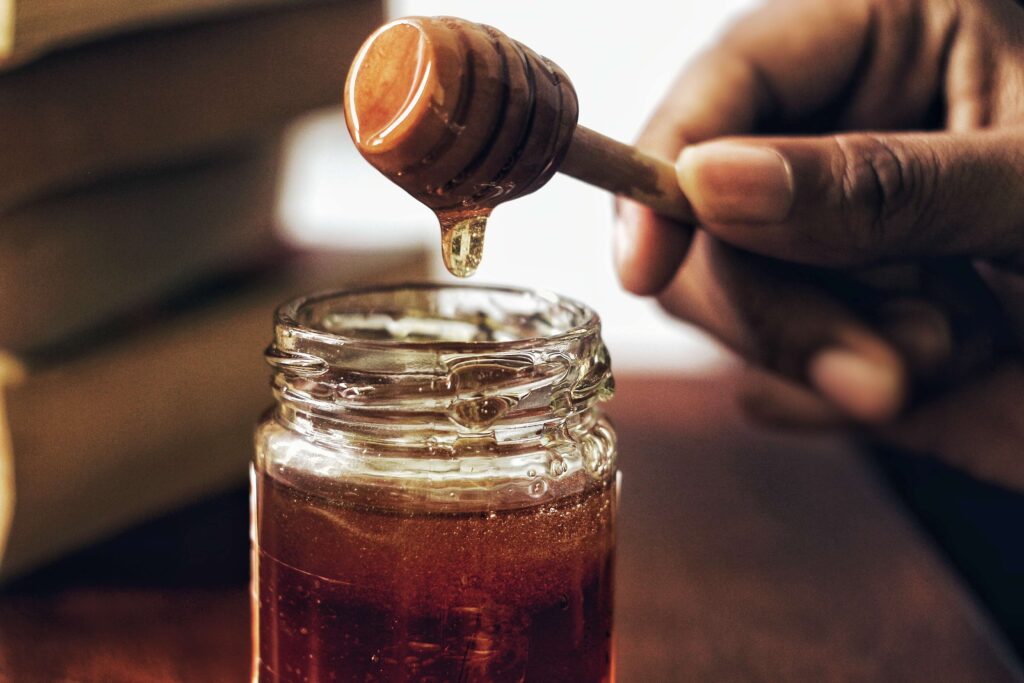 Honey dripping off a wooden honeycomb into a jar full of honey.