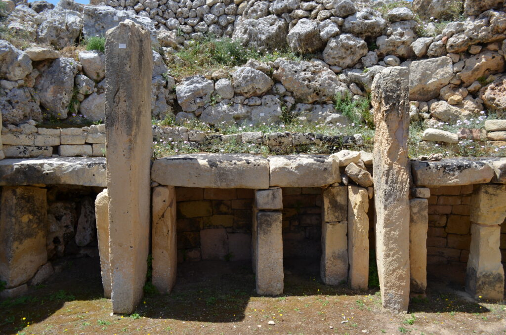 It Tempjital Ggantija, one of MAlta's megalithic temples. Two large, rectangular stones stand upright, framing some medium sized stones, also upright, and topped with rectangular stones arranged horizontally.