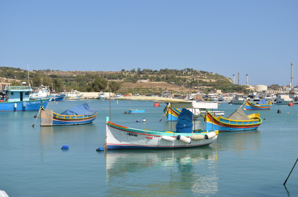 colorful fishing boats, painted bright blue, yellow, and red, sitting in the blue water of the Marsaxlokk harbor.