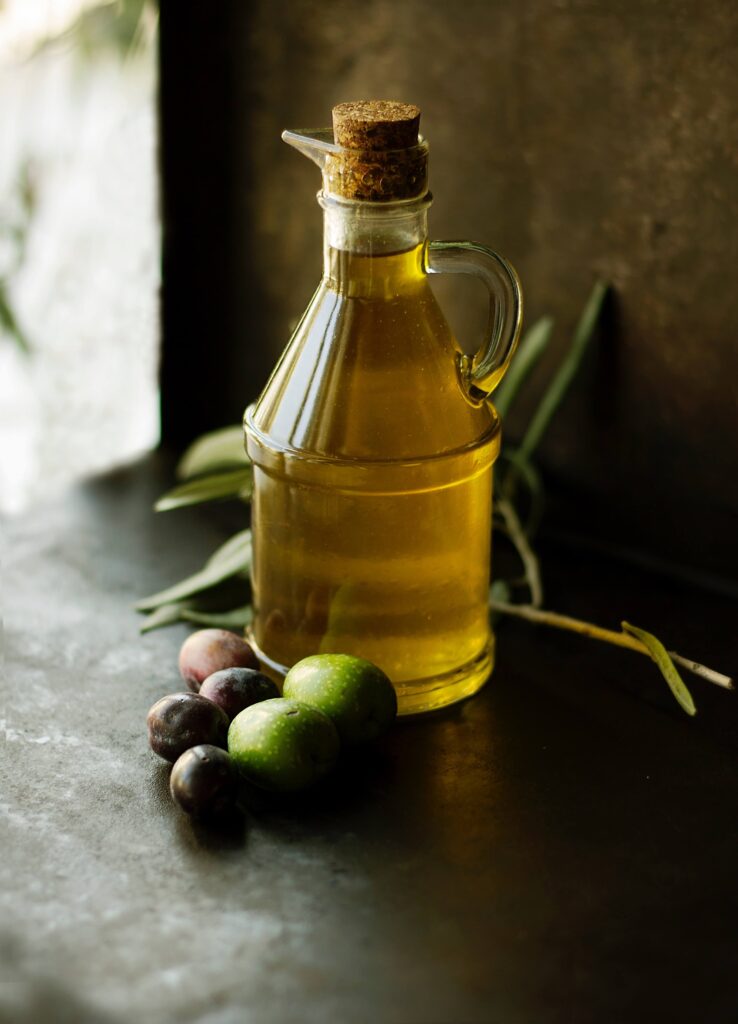 Glass jar of olive oil with cork stopper and fresh olives sitting next to it.