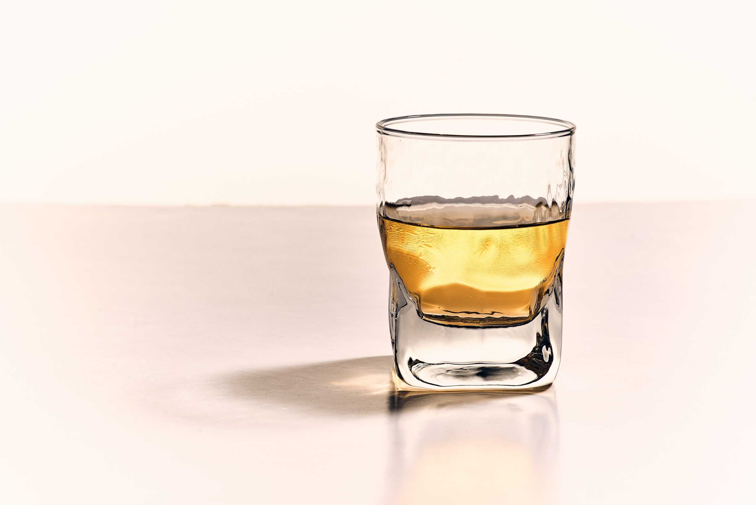 a glass half full with whisky sits atop a beige counter top.