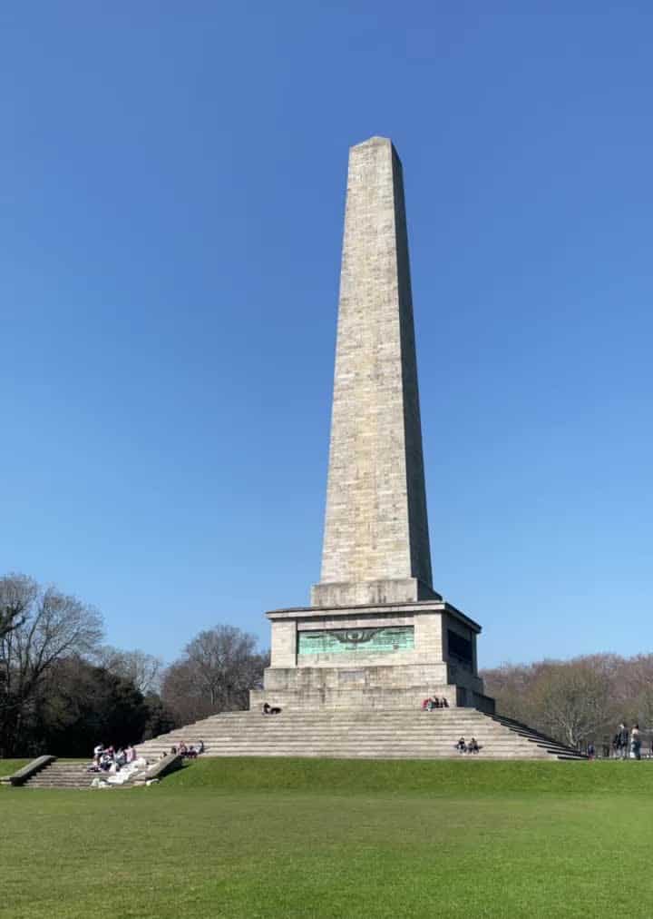 a tall grey stoned obelisk, known as the wellington monument, in a grassy field.