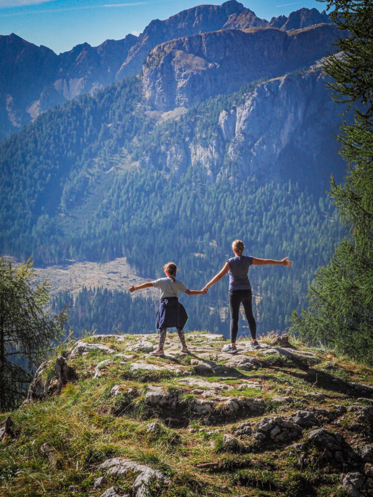 Two people standing with arms outstretched on a rocky outcrop in the Dolomites, celebrating the breathtaking mountain views and the spirit of exploration that encapsulates the essence of hiking in this majestic region.