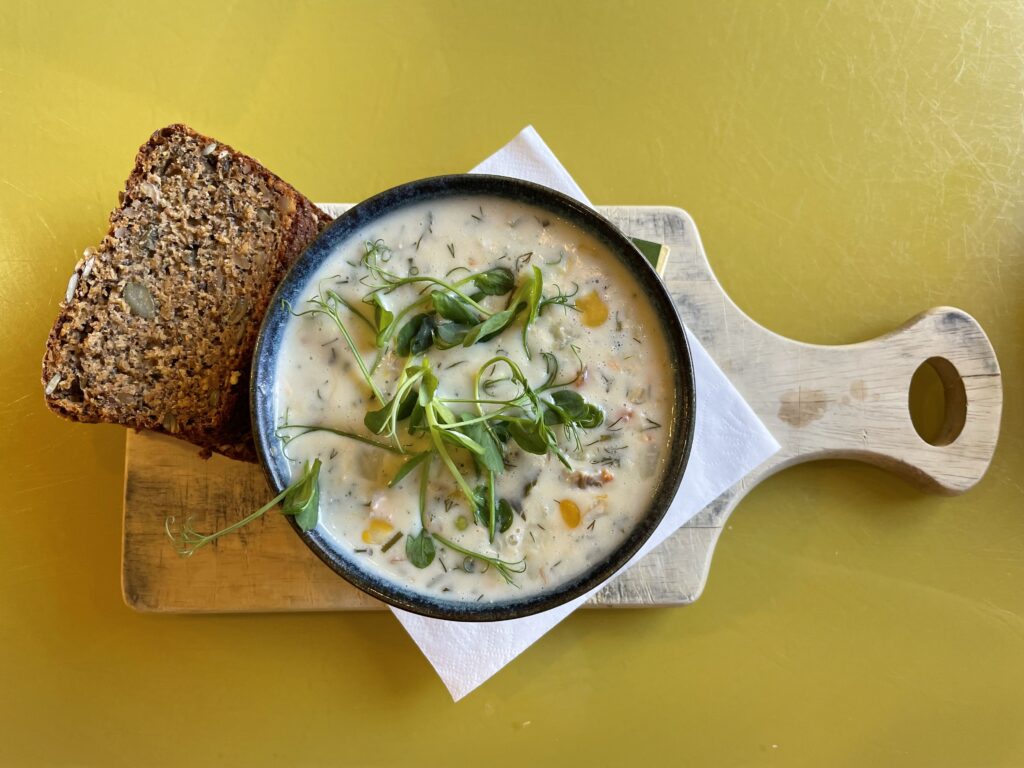 A traditional Irish stew served in a white bowl, featuring tender chunks of fish, carrots, and potatoes, garnished with fresh herbs. The stew is set on a wooden table, suggesting a warm, hearty meal typical of Irish cuisine.