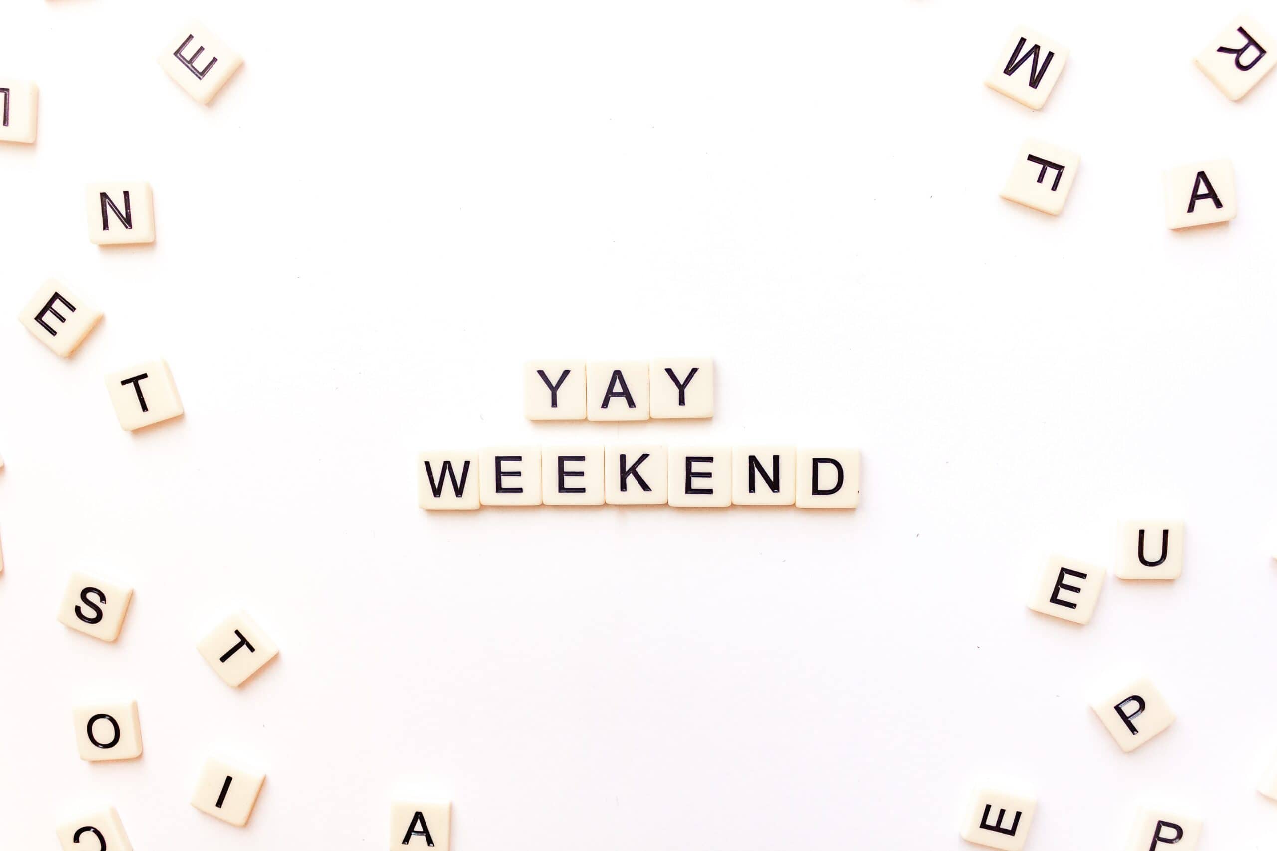 Scrabble tiles on a white surface spelling out 'YAY WEEKEND' surrounded by scattered letters, conveying excitement for the weekend.