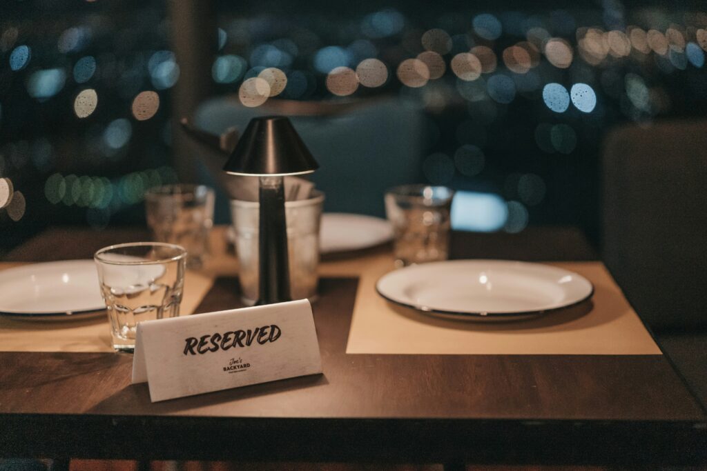 A 'Reserved' sign placed on a table set for two, with a blurred background of city lights, suggesting an intimate evening at a restaurant.