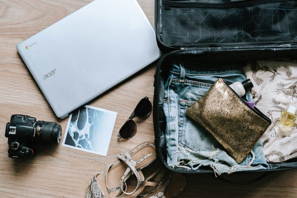 An open suitcase with a casual travel outfit, a gold clutch, sandals, sunglasses, and a DSLR camera, ready for a weekend getaway.