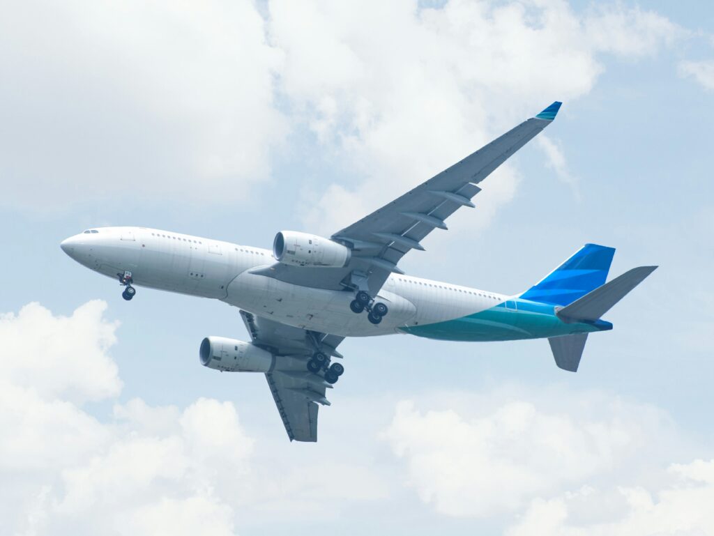 A commercial airplane captured mid-flight against a backdrop of white clouds and blue sky, representing air travel.