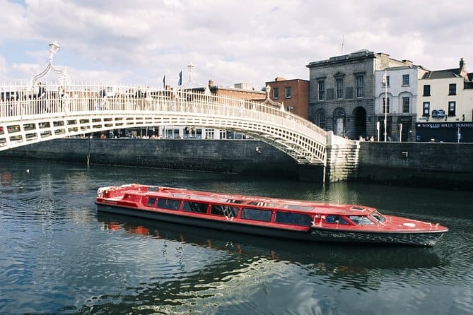 A vibrant red tour boat glides under the iconic Ha'penny Bridge on the River Liffey, offering a picturesque experience often ranked as the best boat Dublin boat tour, set against a backdrop of historic Georgian architecture