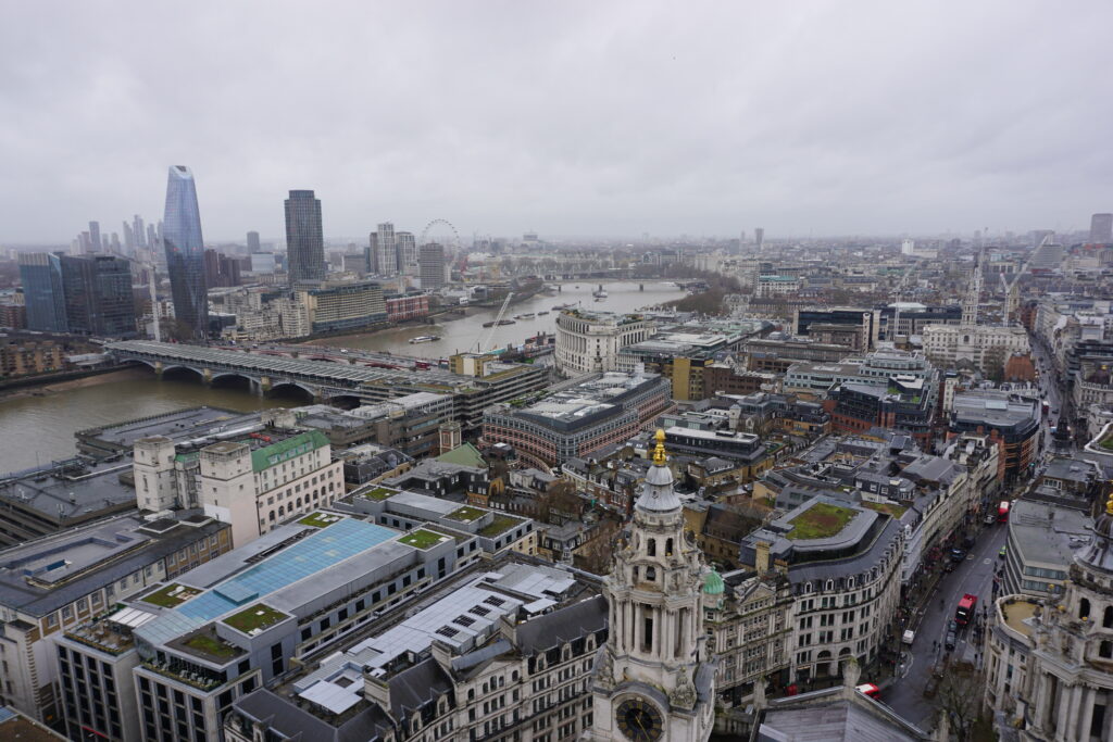 Aerial view of London's cityscape on a cloudy day in London in winter, with the River Thames meandering through the city, flanked by the London Eye and modern skyscrapers.