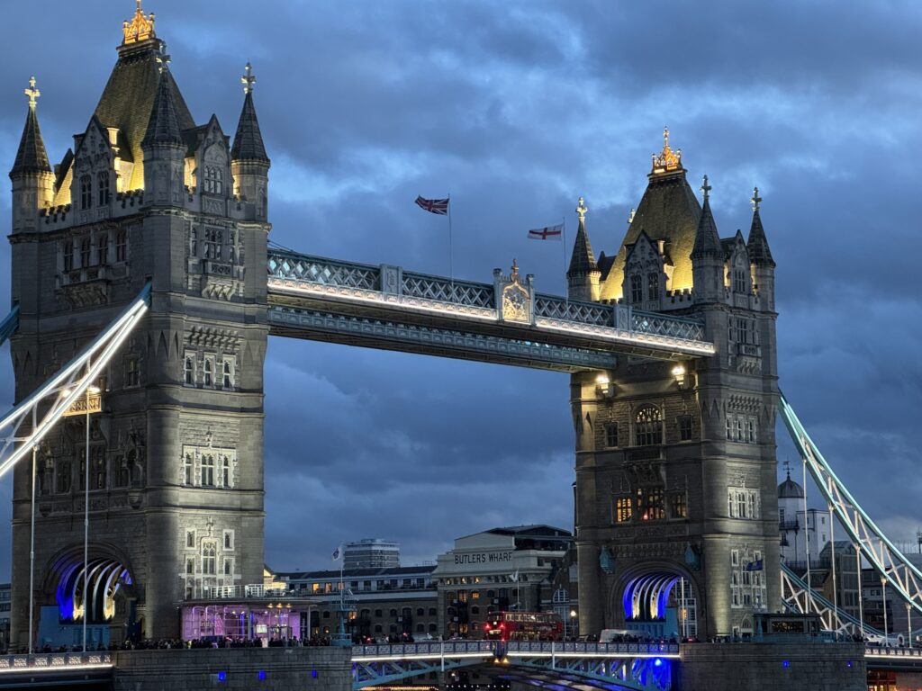 Twilight view of Tower Bridge in London, beautifully illuminated against the evening sky, with the bridge's reflection on the River Thames and the city lights beginning to twinkle.