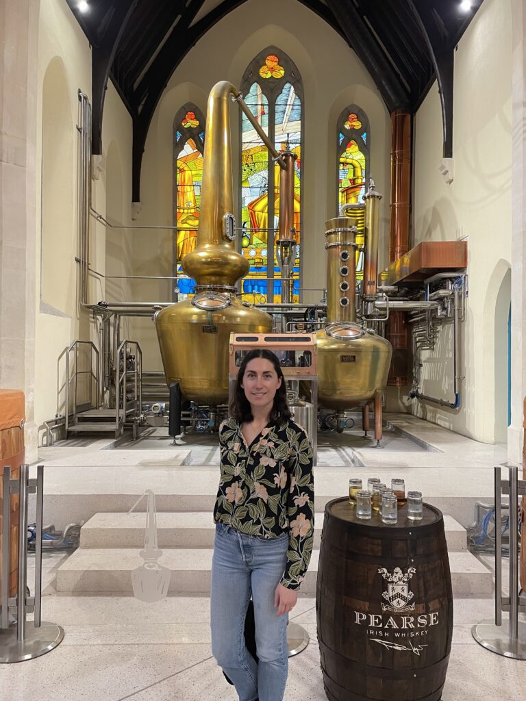 The author, Tamar, smiles in front of gleaming copper stills at Pearse Lyons Distillery, showcasing the intricate whiskey-making process, a highlight of the best whiskey tour in Dublin.