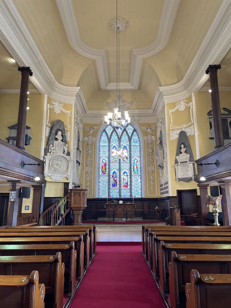 Interior of St. Peter's Church of Ireland showing pews leading to a stained glass window and ornate altar under an arched ceiling.