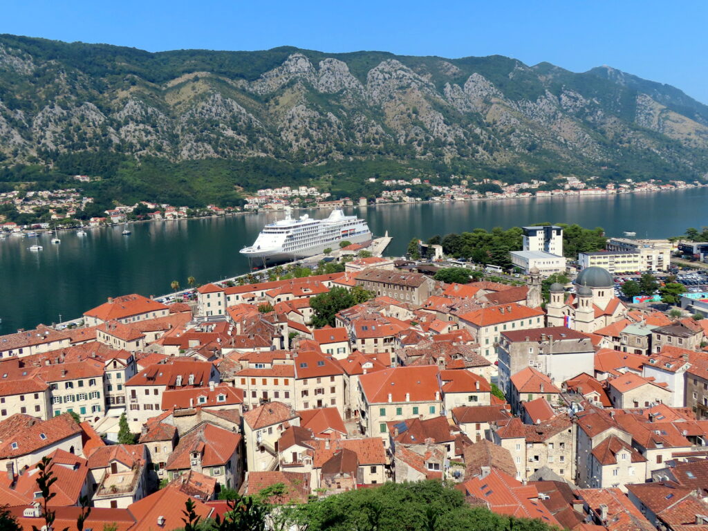 The orange roofed buildings of Kotor's Old Town, with a cruise ship and the Bay of Kotor in the background.