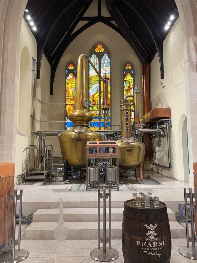 Pearse Irish Whiskey distillery inside a church. Copper stills, stained glass windows, and a whiskey barrel with tasting glasses.