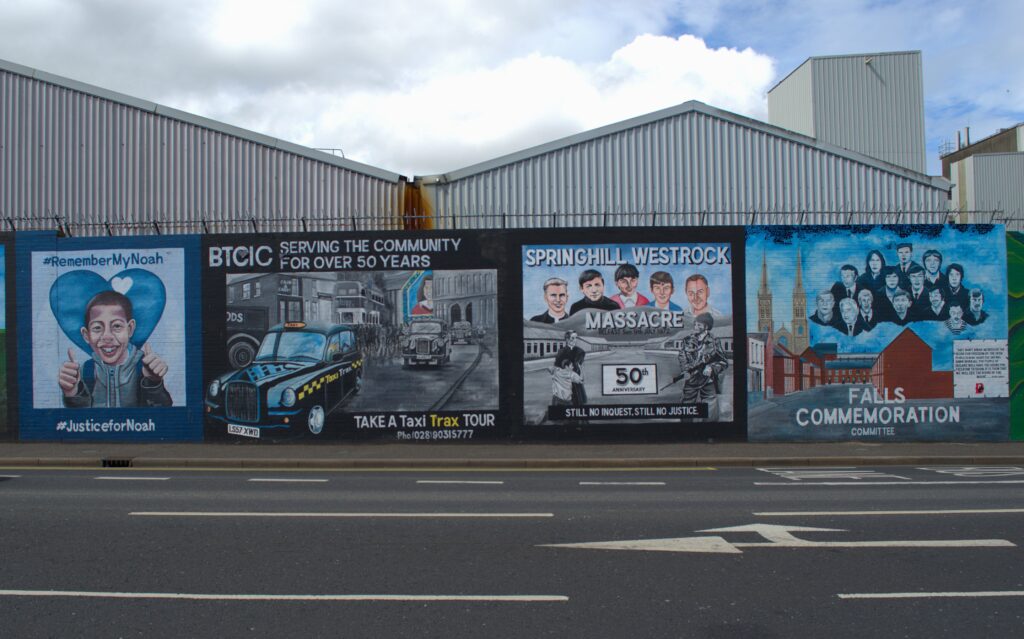 A vibrant mural with four panels: a boy with a thumbs-up, a taxi tour, a tribute to the Springhill Westrock massacre, and a Falls commemoration scene.