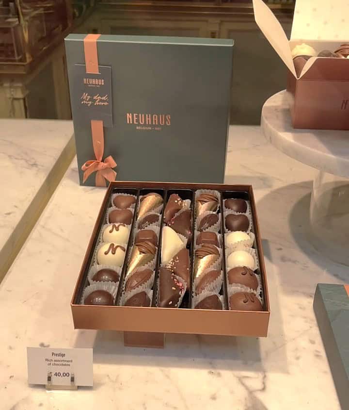 An elegant open box displays an assortment of premium chocolates with diverse shapes and colors on a marble countertop. A price tag reads €40.00.