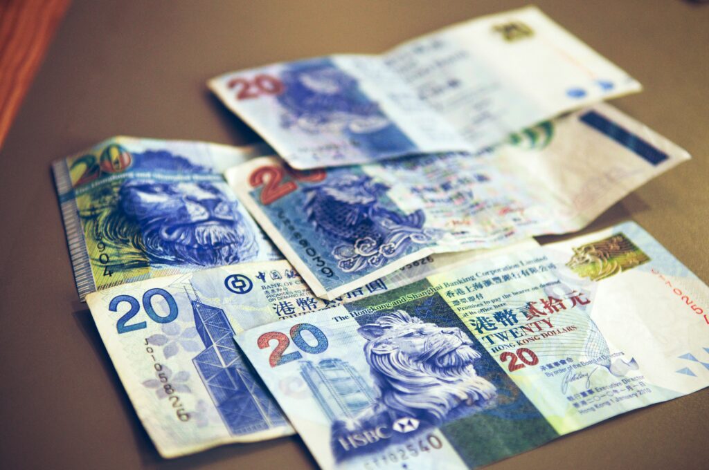 Various denominations of Hong Kong banknotes scattered on a surface, showcasing intricate designs, vibrant colors, and lion imagery, conveying value and detail.